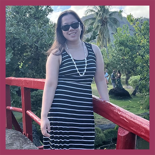 Hannah standing in a striped dress and smiling in a tropical setting
