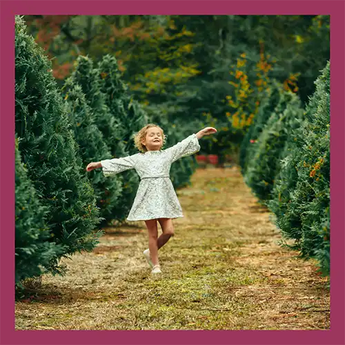 Hartley wearing a dress and dancing in a field full of pine trees