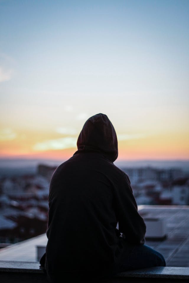 Silhouette of a person in a hoodie sitting and looking at the sunrise