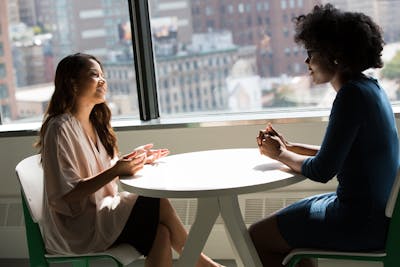 Two women sitting down, facing each other and talking